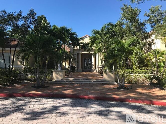 A house entrance with a red brick pathway and palm trees.