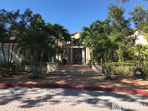 A house entrance with a red brick pathway and palm trees.