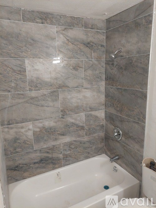 A bathroom with a tub and grey tiles.