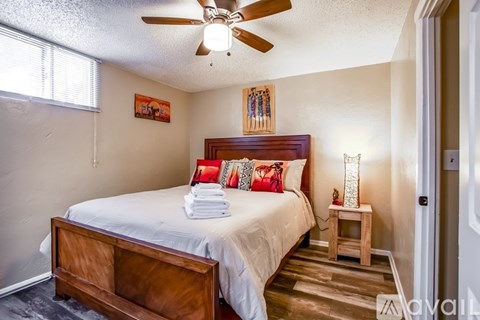 A bedroom with a bed, a ceiling fan, and a small table with a lamp.