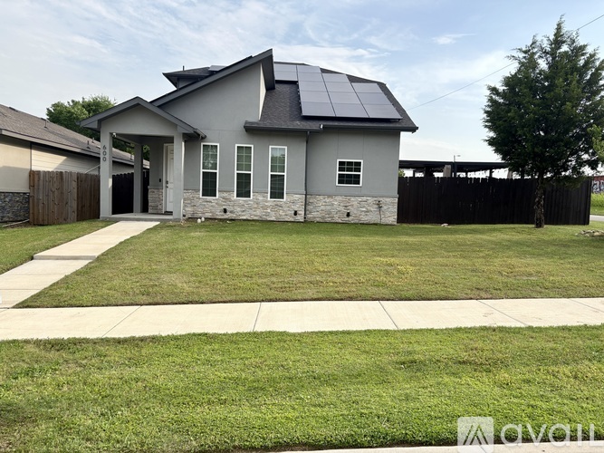 A house with a grey roof and a solar panel on the roof is surrounded by a well-maintained lawn.