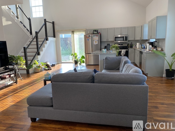A grey couch is in the middle of a living room with a kitchen in the background.