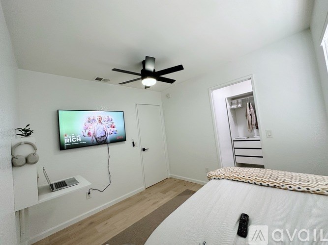 A bedroom with a bed, a television, and a ceiling fan.