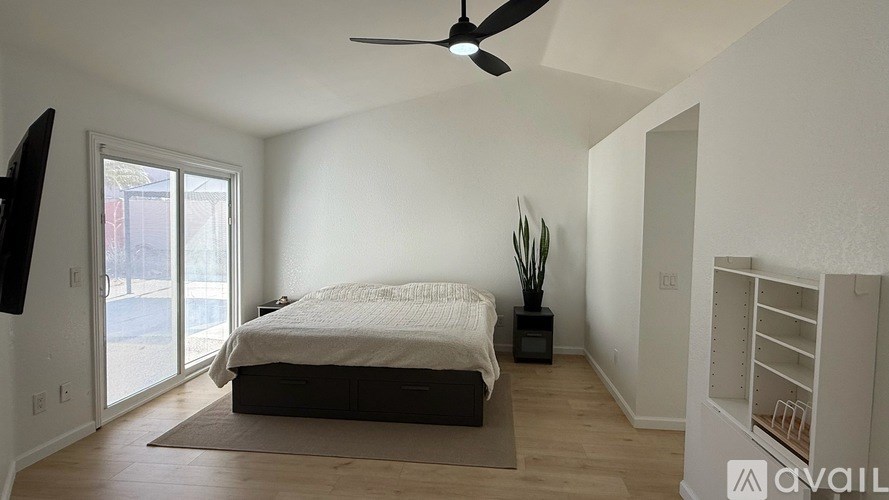 A bedroom with a bed, a ceiling fan, and a sliding glass door.