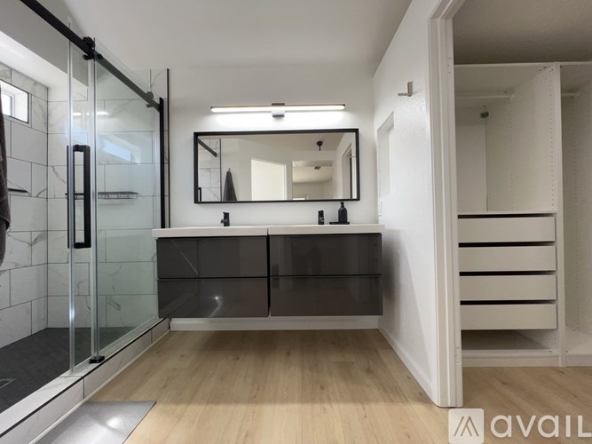 A bathroom with a glass shower door and a wooden floor.