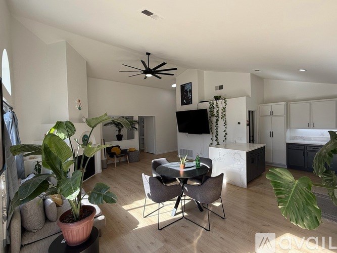 A living room with a dining table and chairs, a potted plant, and a television mounted on the wall.