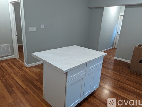 A white kitchen island with a countertop and two doors is in a room with wooden floors.