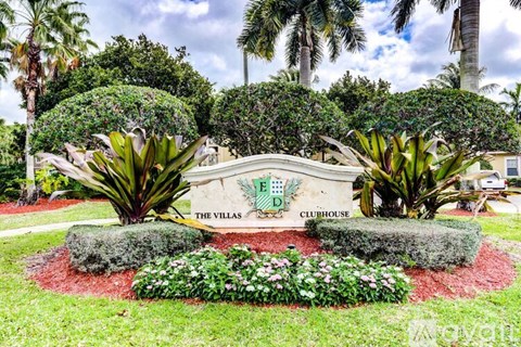 The Villas Clubhouse sign is surrounded by greenery and flowers.