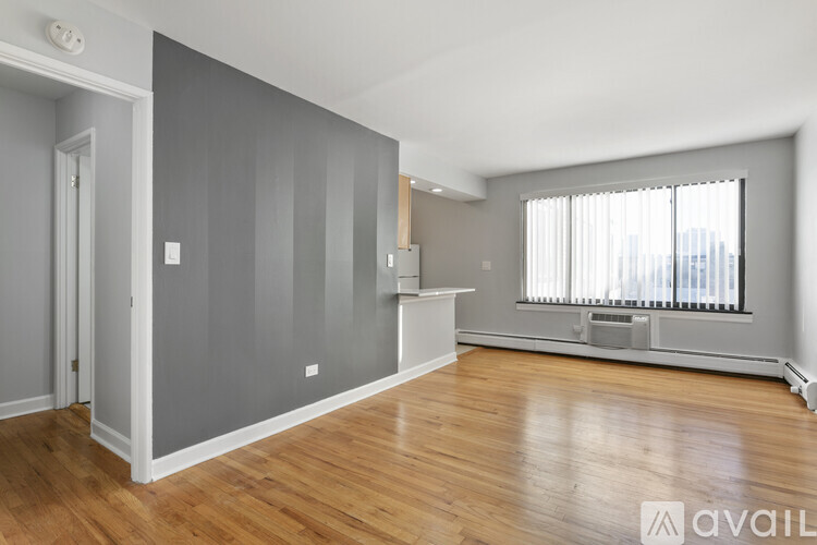 A spacious room with wooden floors and a large window with blinds.