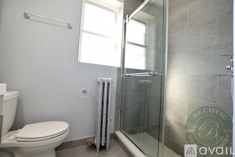 A bathroom with a toilet, a window, and a shower with a glass door.