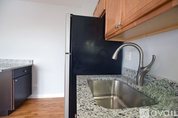 A kitchen with a black refrigerator, granite countertop, and stainless steel sink.