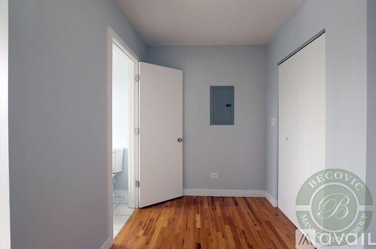 A room with a wooden floor and white walls, with a door on the left and a small window on the right.