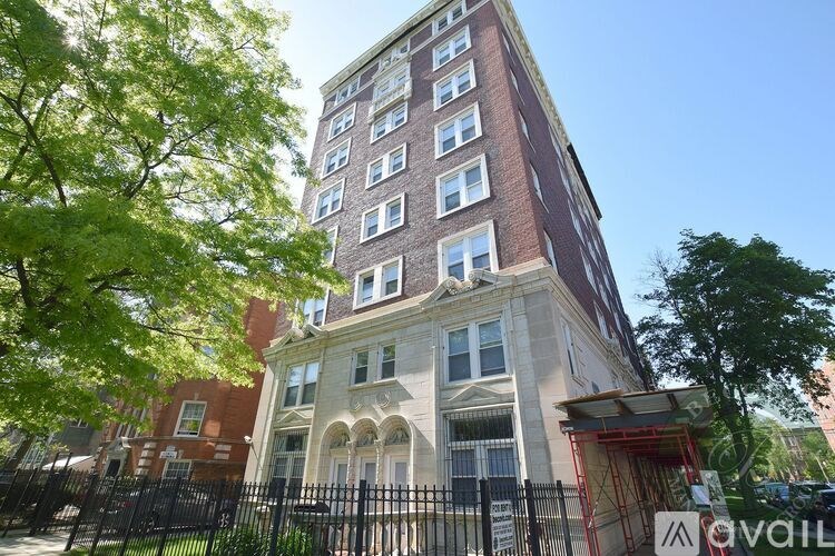 A tall building with a mix of brick and stone facade stands between two trees.