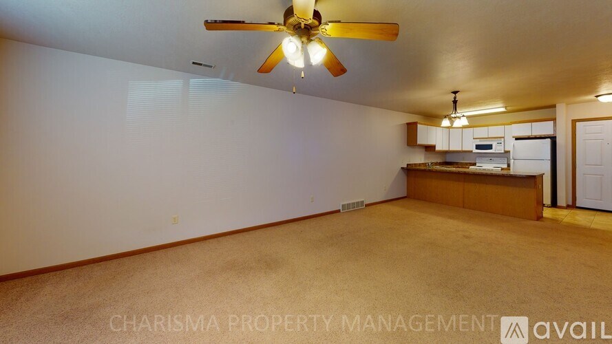 A spacious room with a ceiling fan and a kitchenette in the corner.