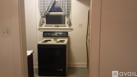 A small black stove sits under a window in a narrow kitchen.