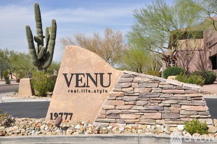 A stone sign with the word VENU and the year 19777 is in the foreground with a cactus behind it.