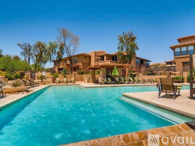 A large swimming pool in front of a house with a patio and chairs.