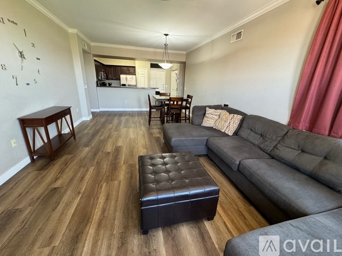 A living room with a grey couch, wooden floors, and a kitchen in the background.