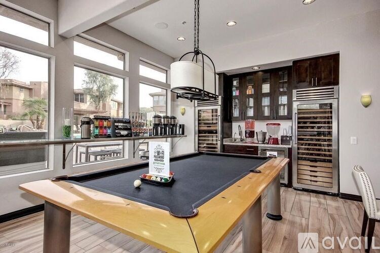 A billiard table is in the middle of a room with a bar and a lot of bottles on the shelves.