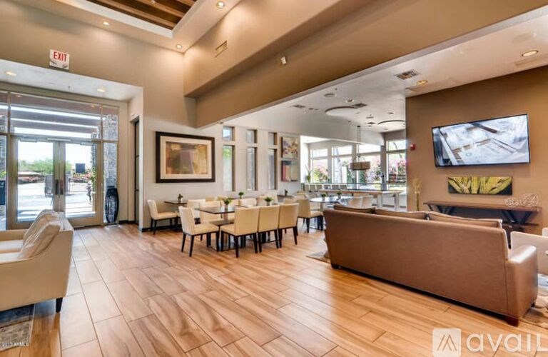 A spacious living room with a brown sofa, white chairs, and a television mounted on the wall.