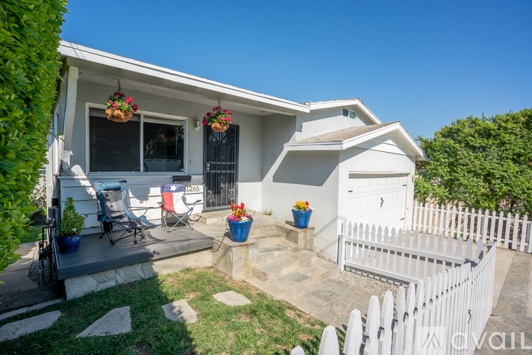 A white house with a white picket fence and a patio with a chair and a table.
