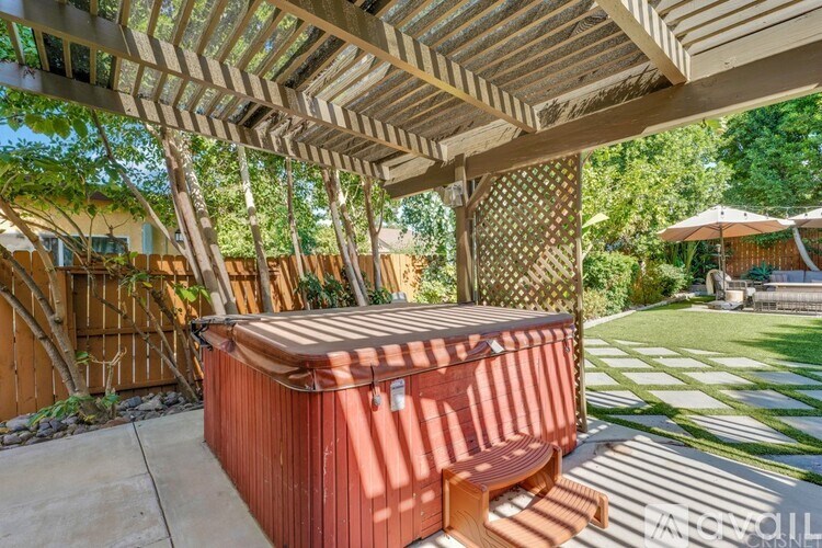 A hot tub sits under a wooden pergola in a backyard.