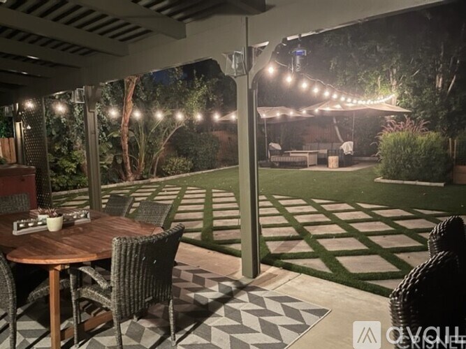 A patio with a table and chairs under a pergola with lights strung up.