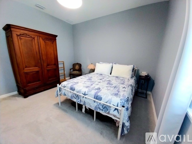 A bedroom with a bed, a wooden armoire, and a nightstand with a lamp.