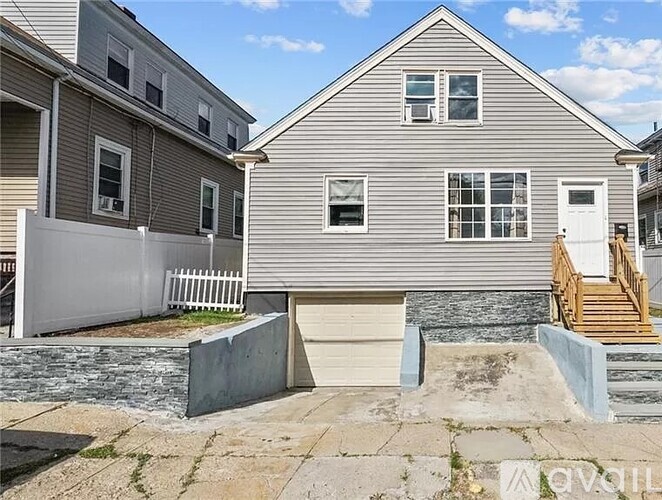 A house with a grey facade and a white door is surrounded by a white fence.