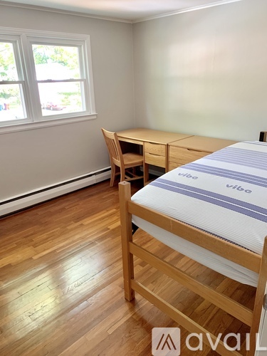 A wooden bed with a striped mattress sits in a room with a desk and chair.