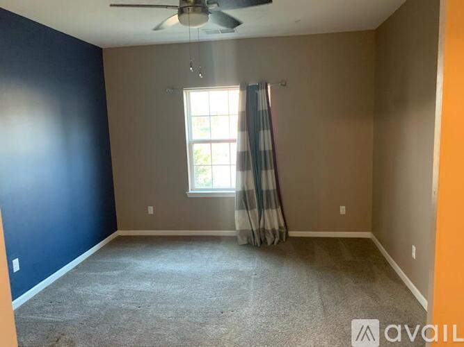 A room with a ceiling fan and a window with curtains.