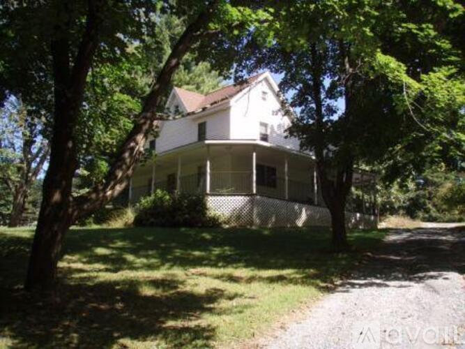 A white house with a porch surrounded by trees.