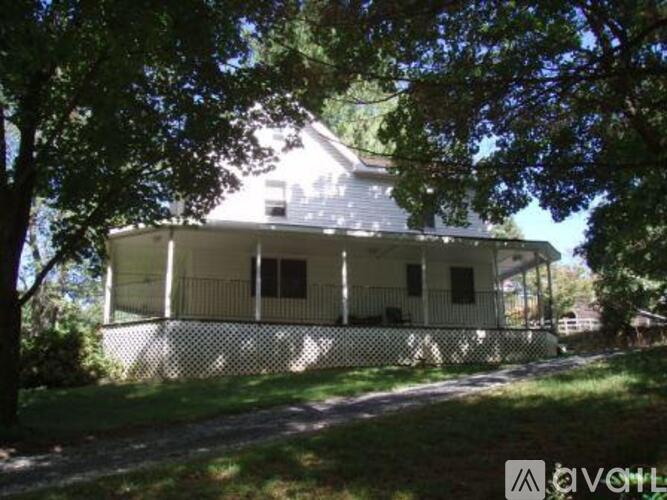 A house with a white fence and a porch is surrounded by trees.