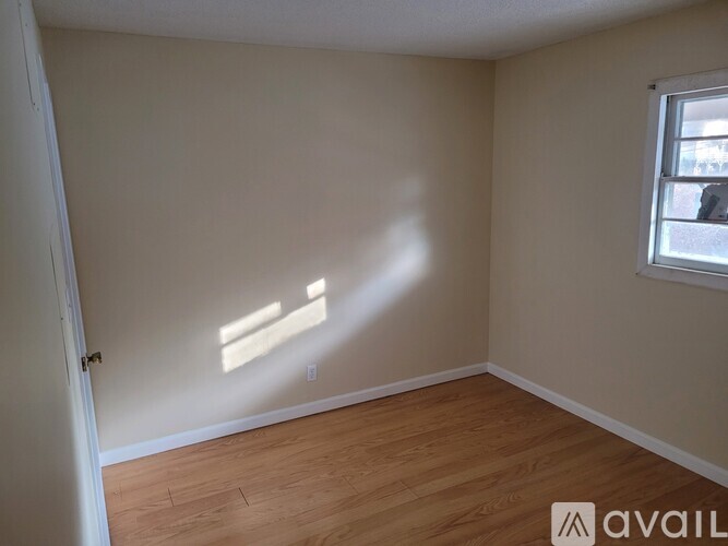 A room with wooden flooring and a window letting in sunlight.