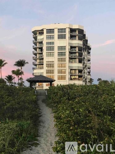 A tall building with balconies is surrounded by greenery and a gazebo-like structure is in the foreground.
