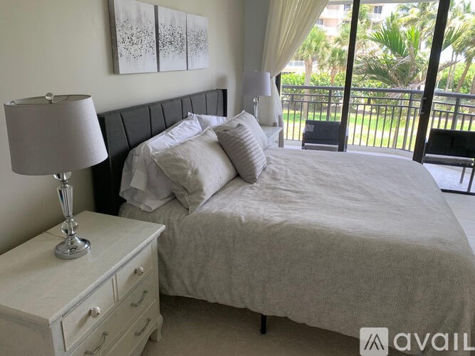 A bedroom with a large bed, a nightstand with a lamp, and a balcony with chairs.