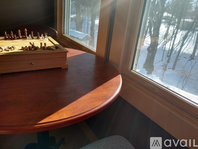 A chess set sits on a wooden table by a window.