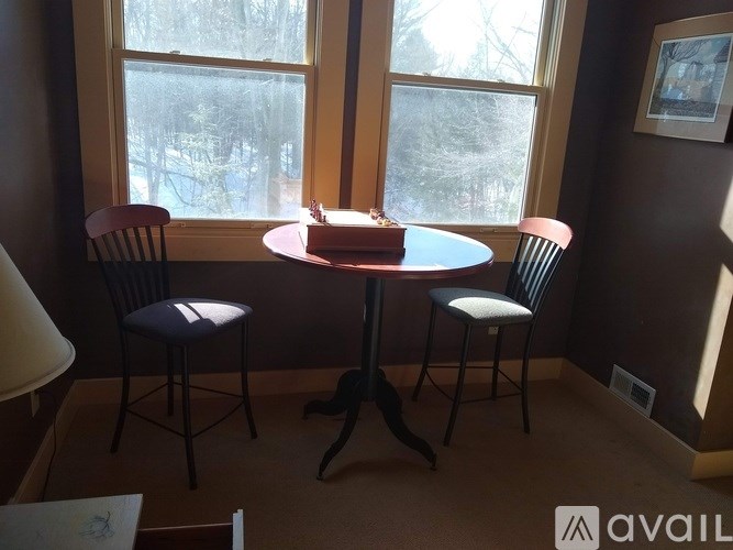 A round table with a cake on it sits in front of a window.