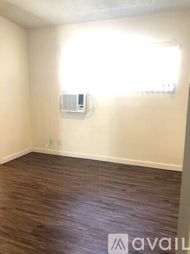 A room with a wood floor and a window with a white air conditioner on the wall.