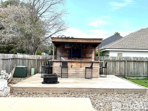 A wooden outdoor kitchen with a grill and chairs.