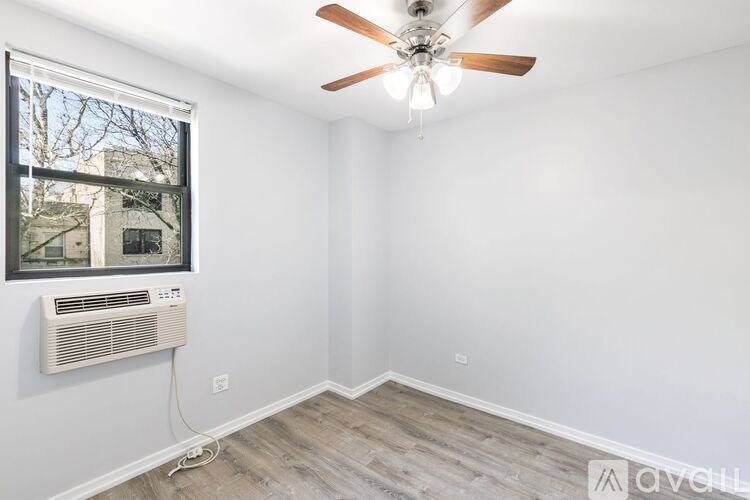 A room with a ceiling fan and a window with an air conditioner unit.