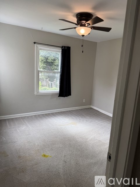 A room with a ceiling fan and a window with a view of trees and a fence.