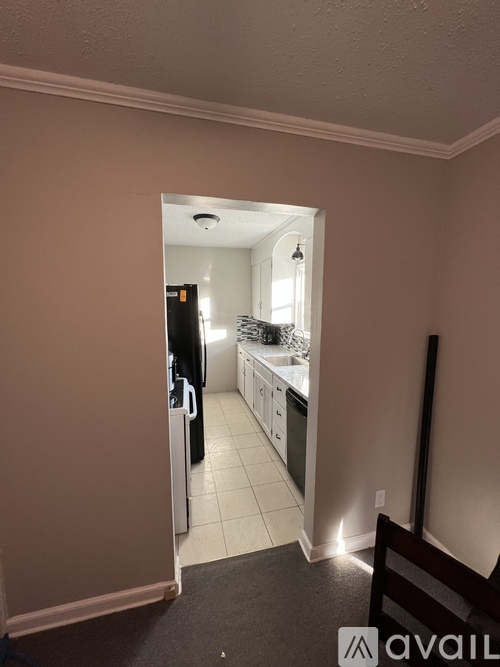 A kitchen with a refrigerator, sink, and cabinets is visible through an open door.