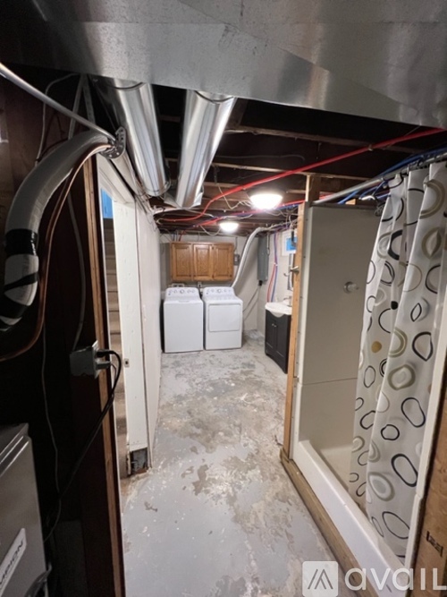 A narrow hallway with a lot of pipes and a door on the left.