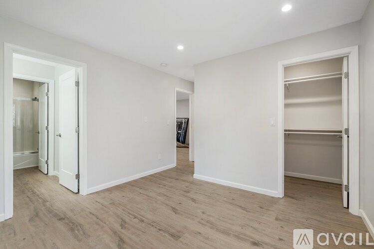 A spacious room with white walls and wooden flooring, featuring a large open doorway and a built-in closet.