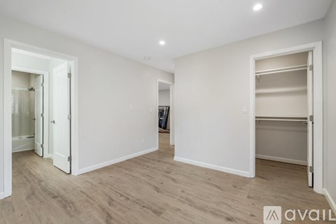 A spacious room with white walls and wooden flooring, featuring a large open doorway and a built-in closet.