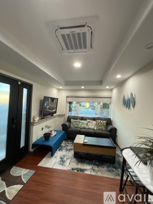 A living room with a black couch, a blue ottoman, and a wooden coffee table.
