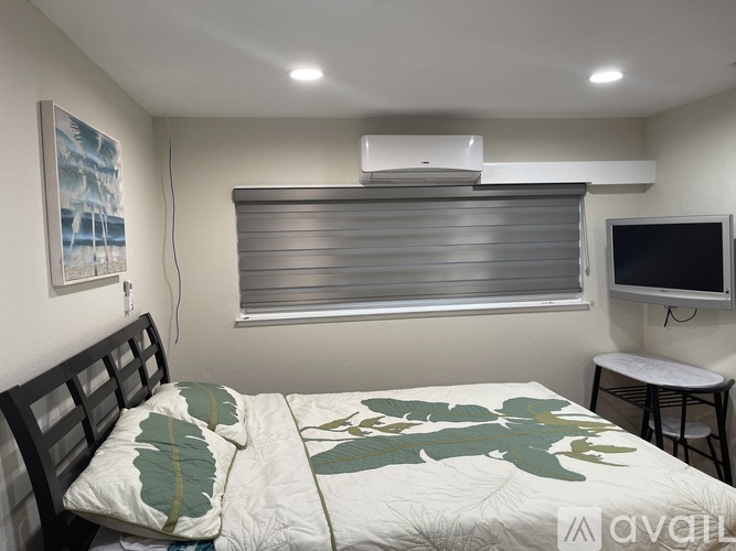 A bedroom with a bed, a small table, and a window with blinds.