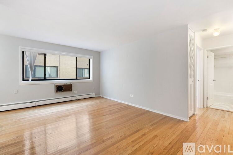 A spacious room with wooden flooring and a large window with a view of a building outside.