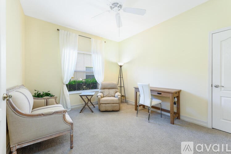 A living room with a sofa, chair, desk, and a fan.